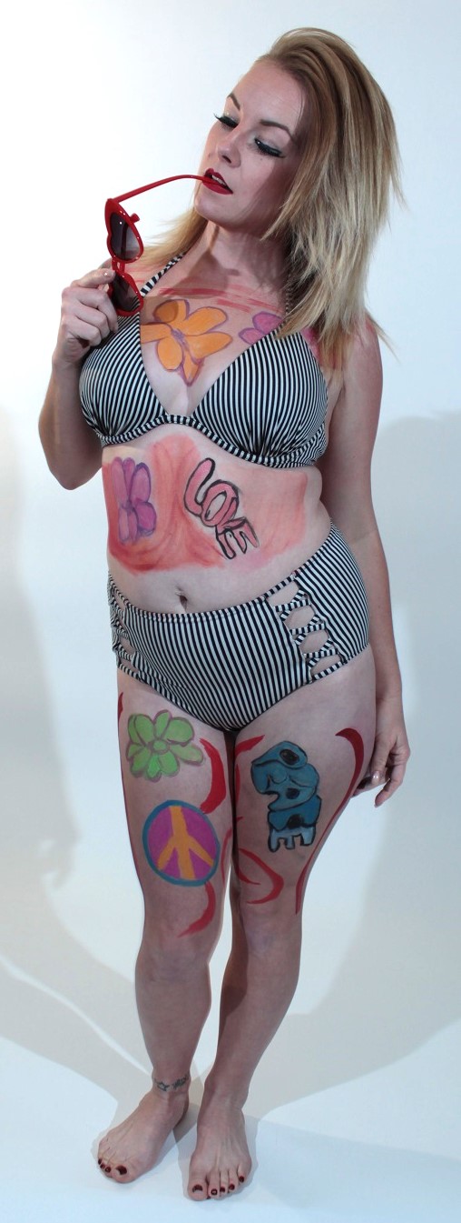 model dressed as a 60s go-go girl dancer with era flowers on her chest, stomach and leg, a peace sign on her right leg, the word peace on her left leg and the word love on her stomach 