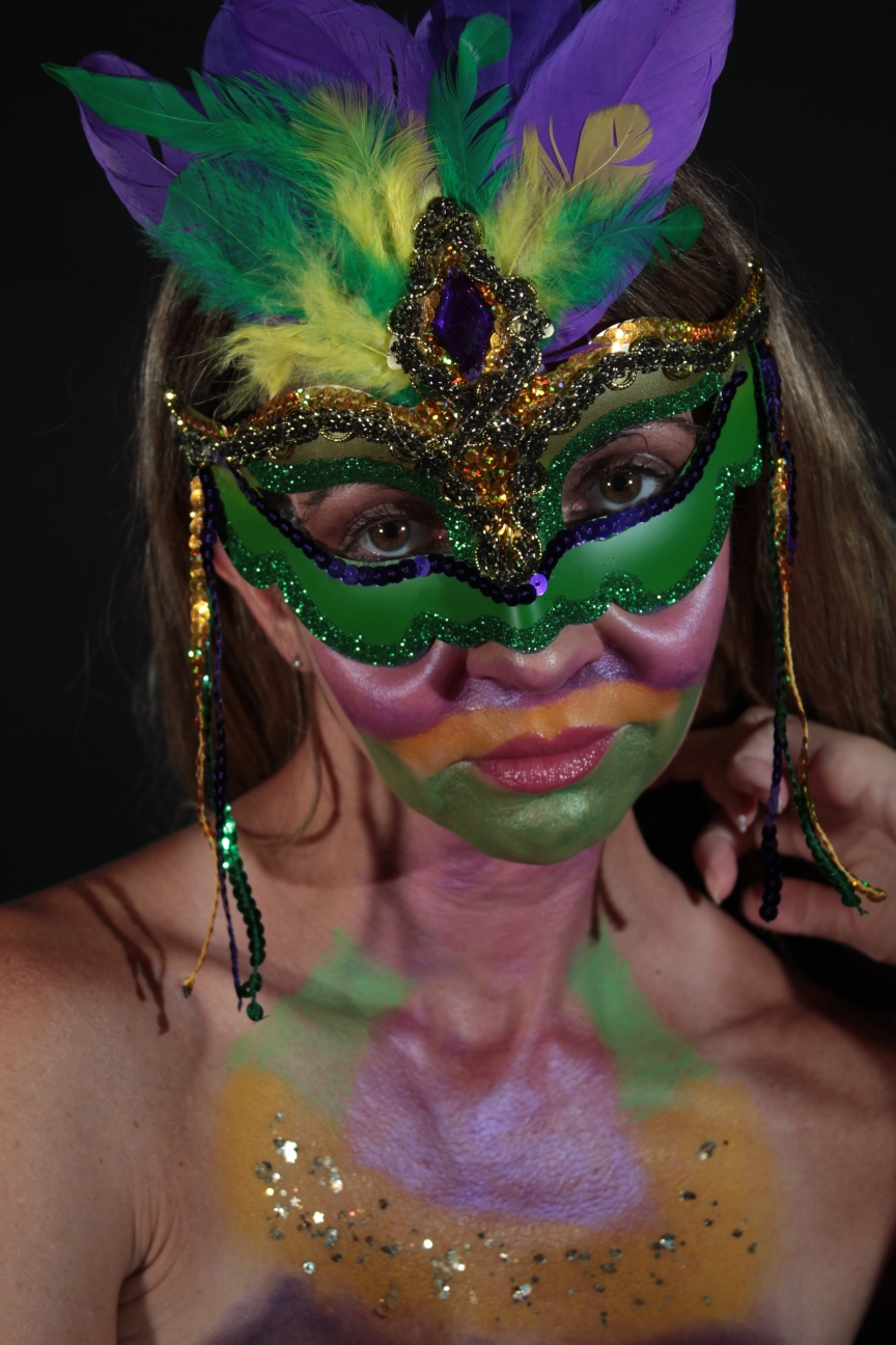 Model wearing Mardi Gras mask and face painted in Mardi Gras colors