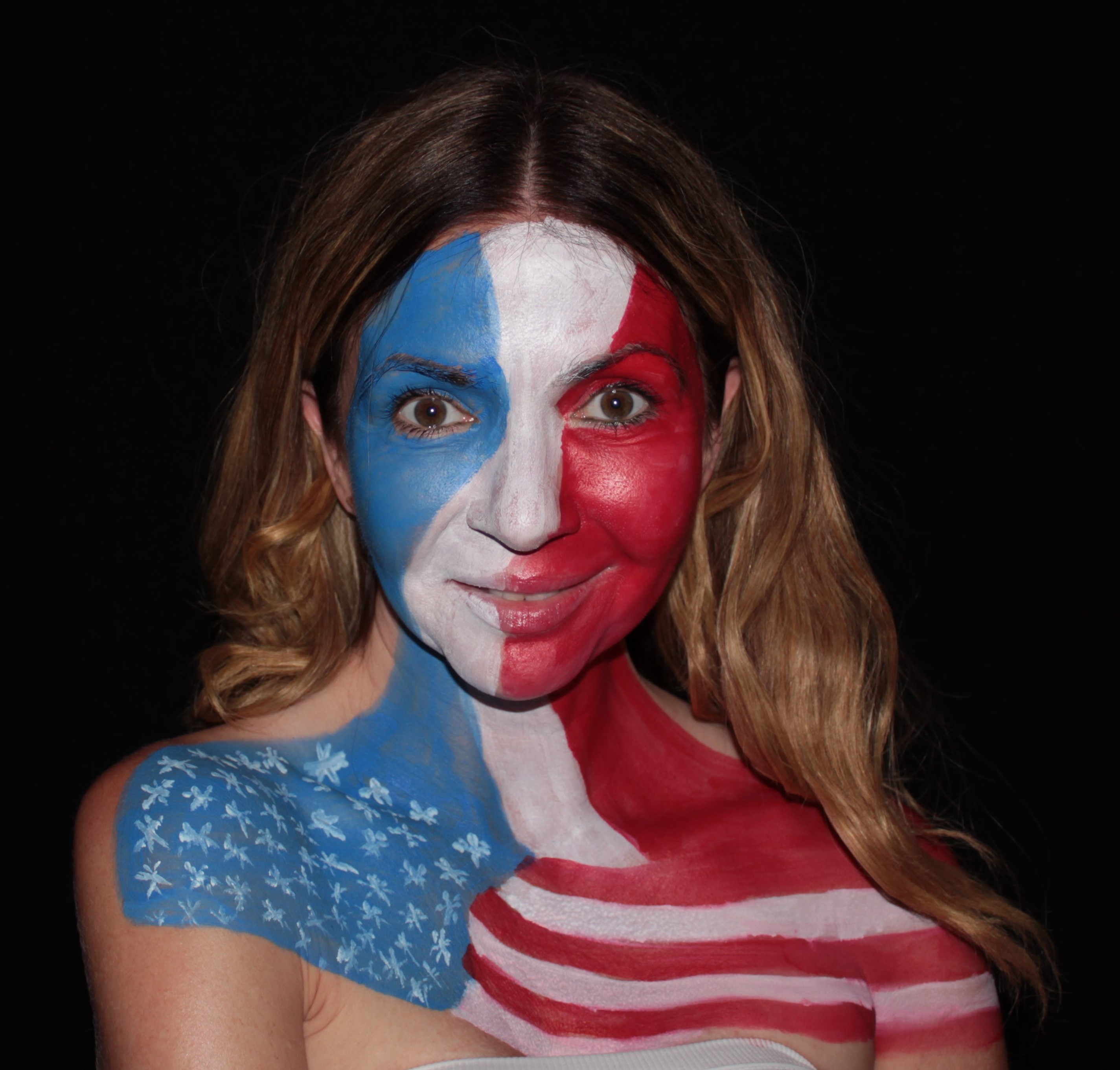 woman's face painted with vertical blue, white, red stripes. Across her shoulders is painted an American flag
