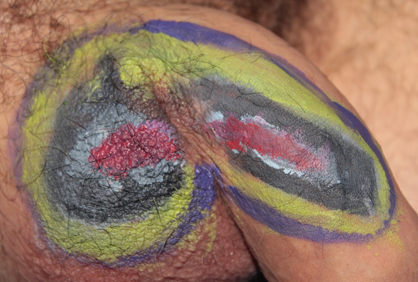 body painting on penis of oval shape on side of penis and scrotum: purple outter line, yellow inside that, purple inside that and pink at center