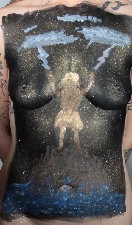 body painting on female torso of gold silhouette of woman on rocks surrounded by crashing waves, with lightning coming out of the clouds