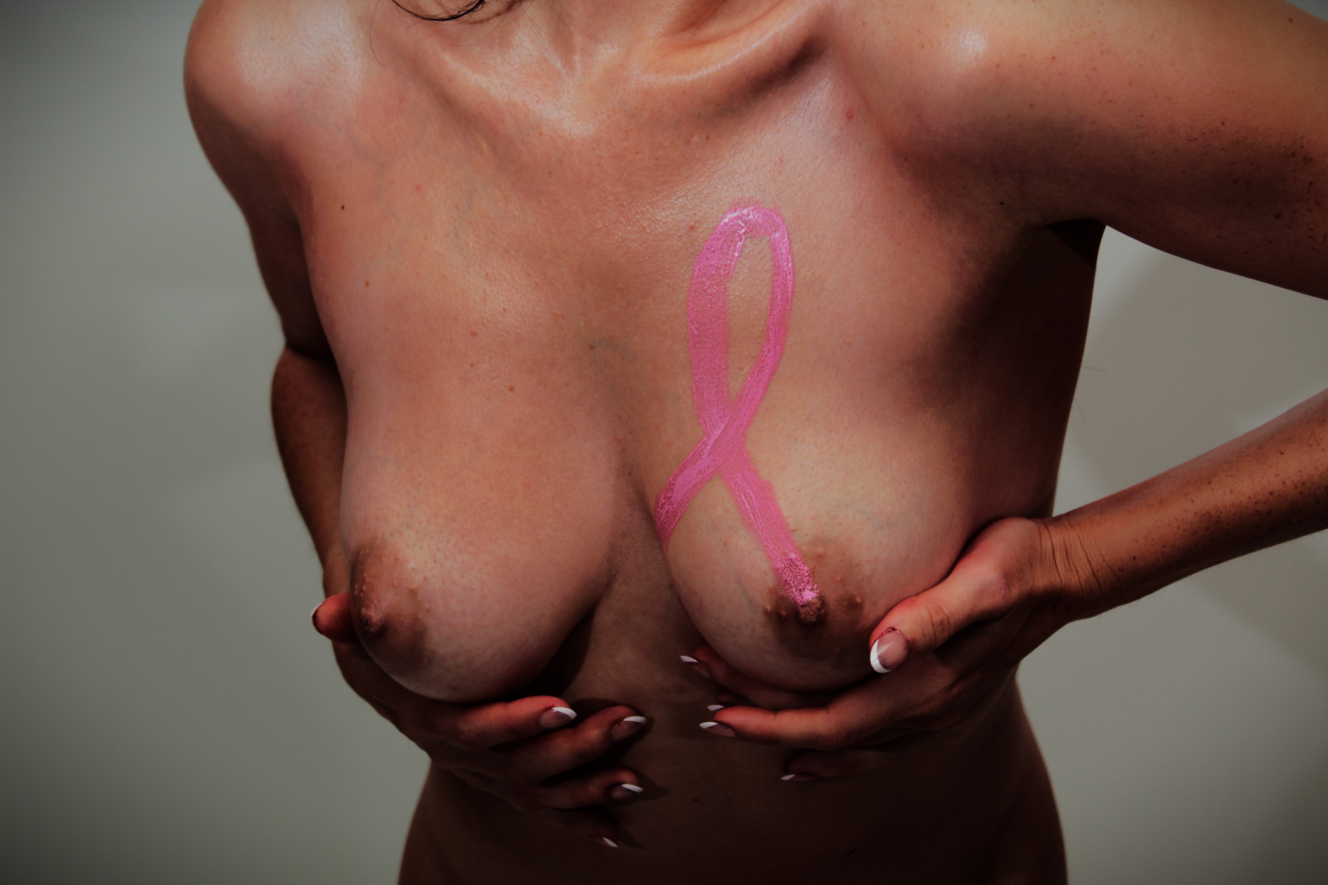 body painting of pink ribbon on woman's left breast