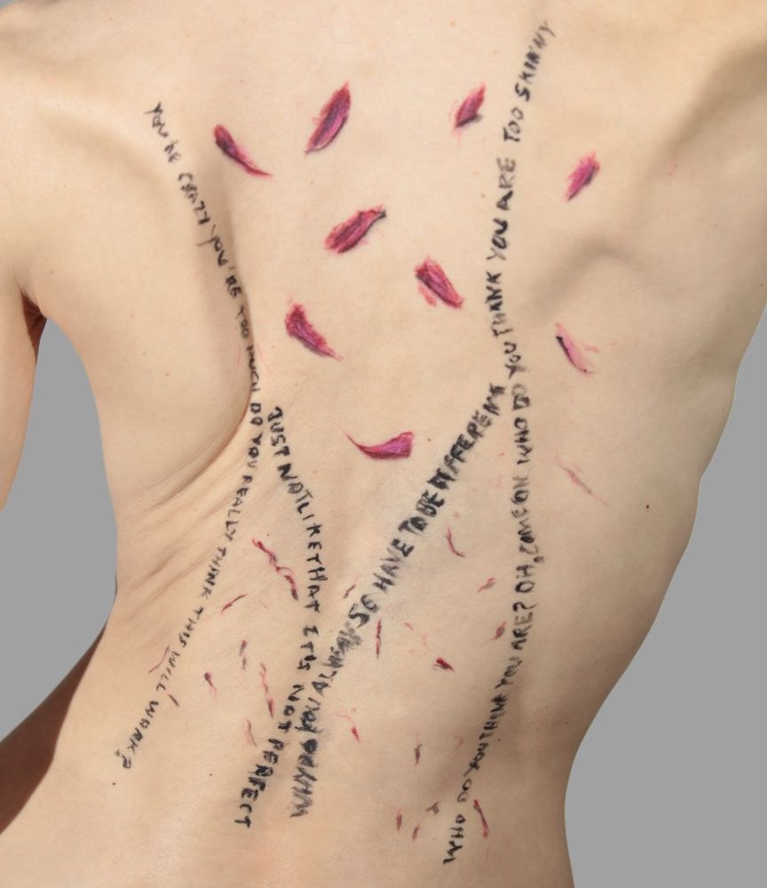 model with words written on her back along with a few body painted red rose petals