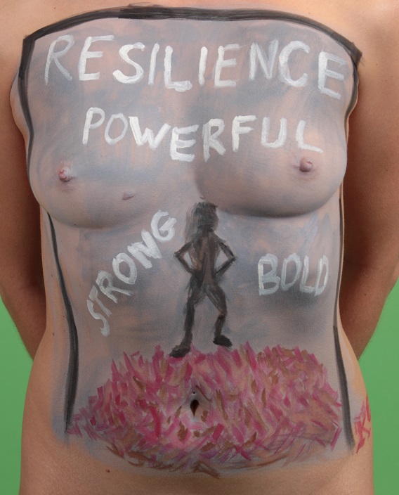model with the words, Resiliance, Powerful, Bold, Strong, painted on her torso with a silhouette of a woman standing on a pile of bricks on her stomach